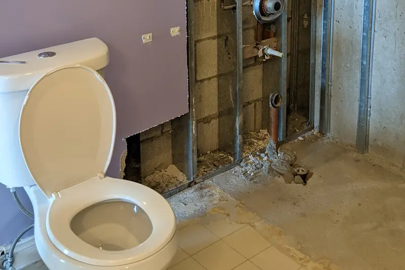 A bathroom wall beside a toilet opened down to the metal studs and old backing during a remodel
