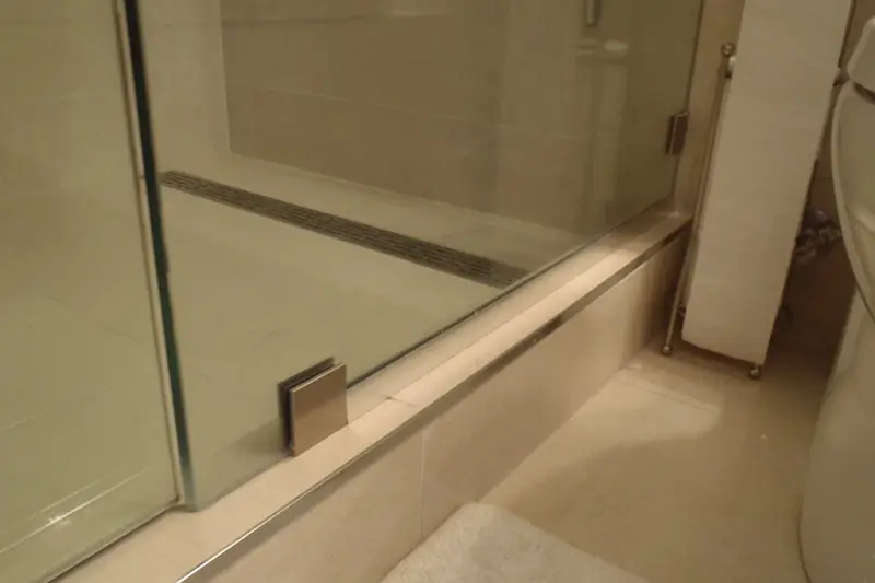 A slim linear drain running the width of a tiled walk-in shower behind a frameless glass door