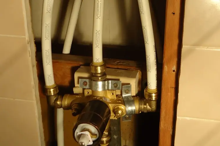 A brass shower valve body in an open stud bay with white plastic supply lines connected to it, waiting for the wall to be closed