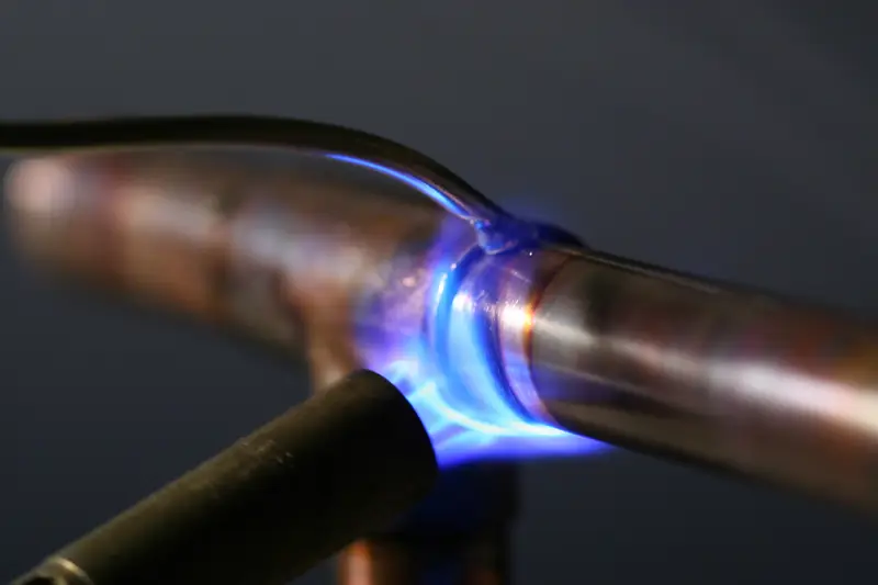 A torch flame heating a copper pipe joint while it is soldered