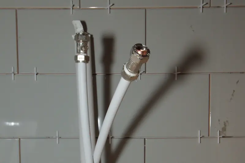 White plastic water supply stubs with threaded ends sticking out in front of a bare tiled wall, waiting for the fixture