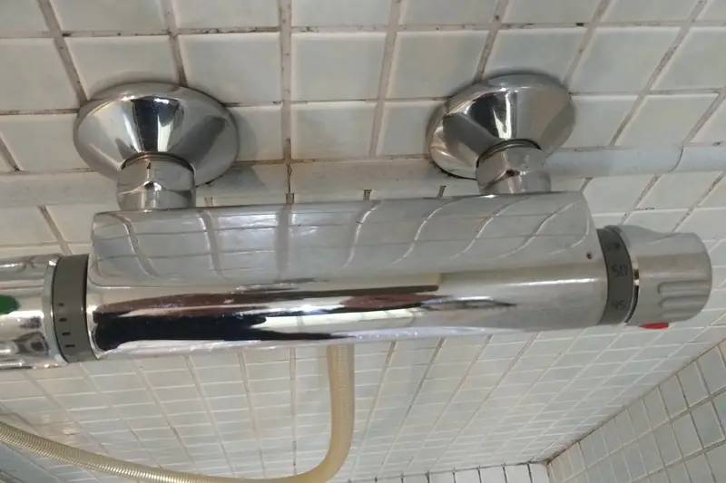 Chrome bar-style thermostatic shower valve mounted on a tiled wall, temperature dial at one end